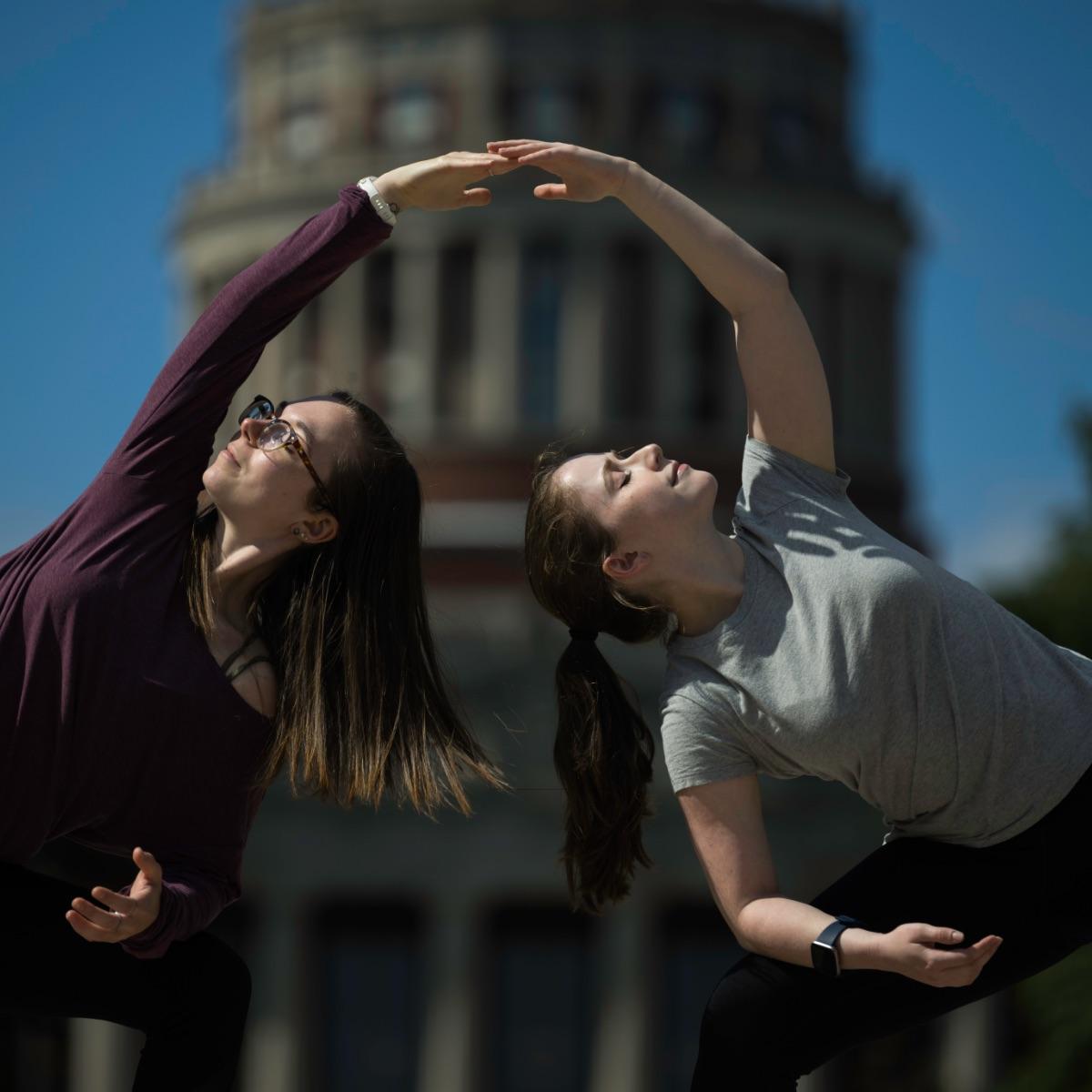 Two students side bend towards each other so their hands meet on the quad